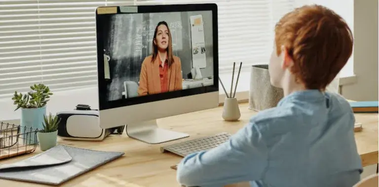 Schüler sitzt vor dem Computer und redet mit seiner Lehrerin