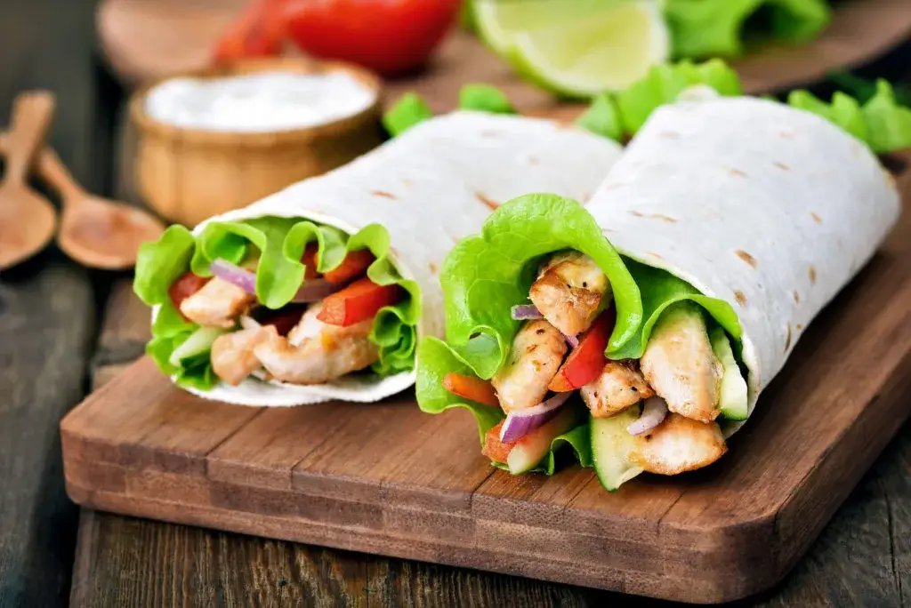 2 Wraps mit Salat, Zwiebel, Tomaten und Hänchen auf einer Holzplatte