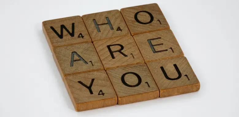 Der Satz "Who are you", gebildet durch Holzbuchstaben des Scrabble-Spiels, weist auf die Bedeutung von Charaktereigenschaften für Bewerbungen hin.