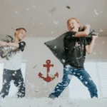Zwei Kinder stehen auf dem Bett und machen eine Kissenschlacht