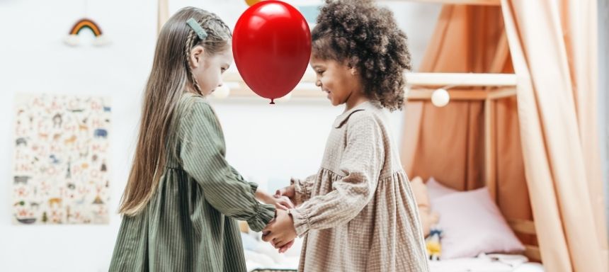 zwischen der Stirn zweier Mädchen ist ein Ballon, sie halten sich an den Händen