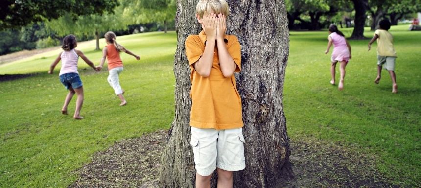 Kind in der Mitte steht hinter Baumstamm und hält sich die Augen, je 2 Kinder pro Seite rennen weg