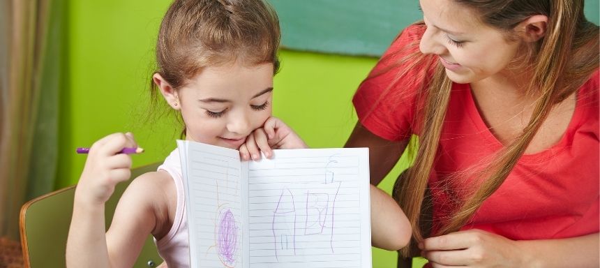 Frau sieht Mädchen an, dass eine Zeichnung von sich in einem Heft zeigt