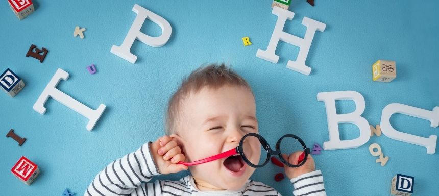 Kind hat Brille in den Händen und liegt auf hellblauem Hintergrund mit vielen Buchstaben