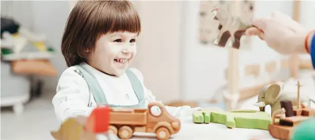 Eine Person hält ein Spielzeug hoch und ein ADS Kind lächelt.