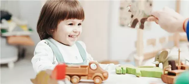 ADS Kinder Symptome Darauf solltest du Achten Eine Person hält ein Spielzeug hoch und ein ADS Kind lächelt.