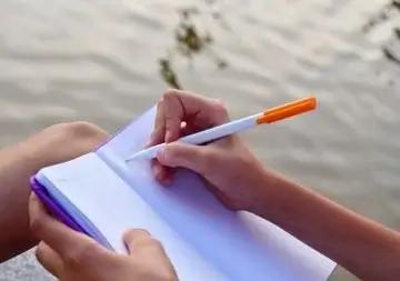 Eine Person schreibt mit einem Kugelschreiber etwas in ein Notizbuch