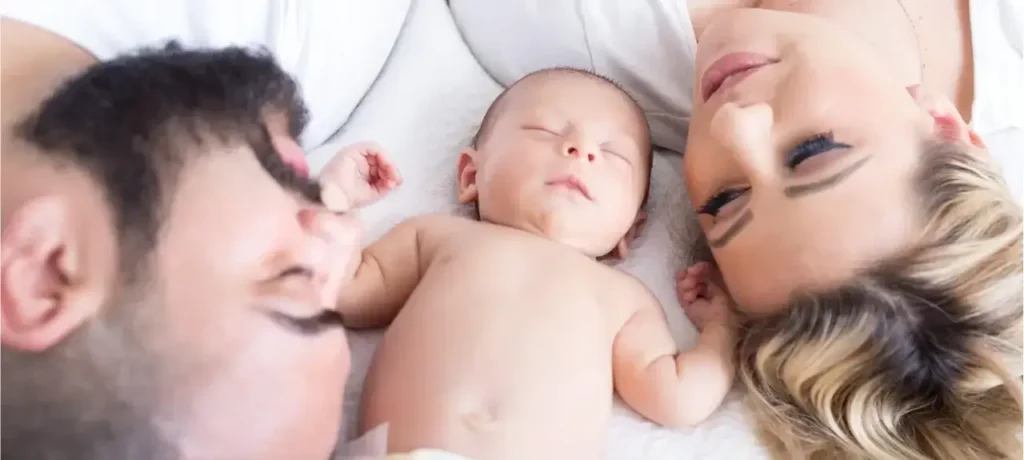 Ein Baby liegt schlafend zwischen Mutter und Vater als Bindungspersonen.