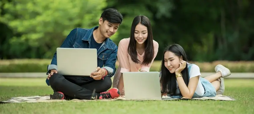 3 Schüler lernen auf einer Wiese gemeinsam