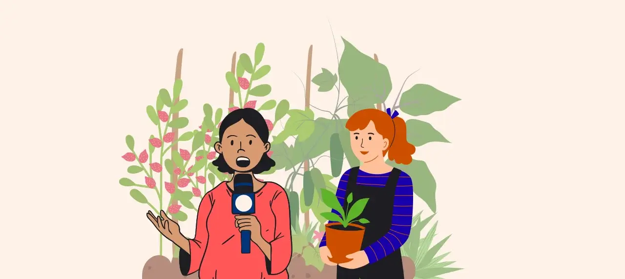 Im Vordergrund zwei Frauen. Linke Frau hat ein Mikrofon. Rechte Frau hält eine Pflanze. Im Hintergrund ein Blumenbeet.