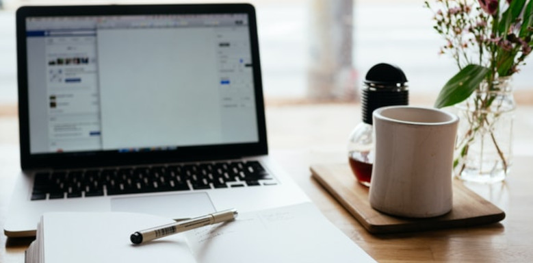 Laptop, Tasse und Notizbuch auf dem Tisch