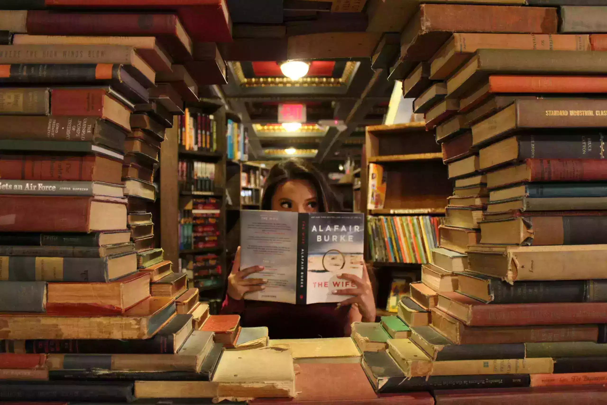 Junge Frau sitzt mit einem Buch in einer Bibliothek